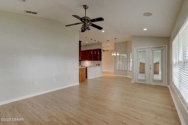 unfurnished living room with vaulted ceiling, ceiling fan with notable chandelier, french doors, and light wood-type flooring