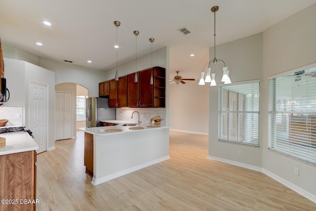 kitchen featuring backsplash, sink, hanging light fixtures, light wood-type flooring, and stainless steel fridge