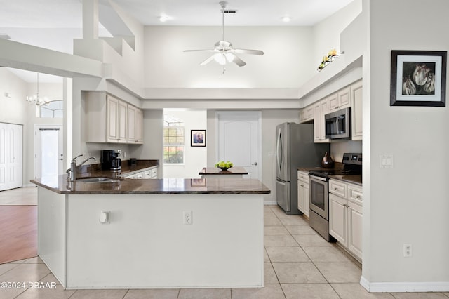 kitchen featuring a towering ceiling, kitchen peninsula, appliances with stainless steel finishes, and sink