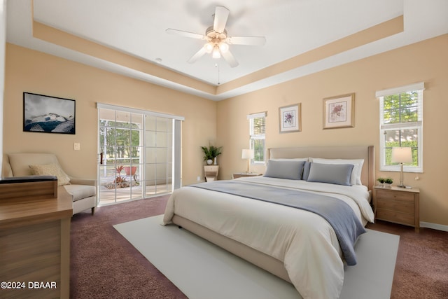 carpeted bedroom with access to exterior, ceiling fan, and a tray ceiling