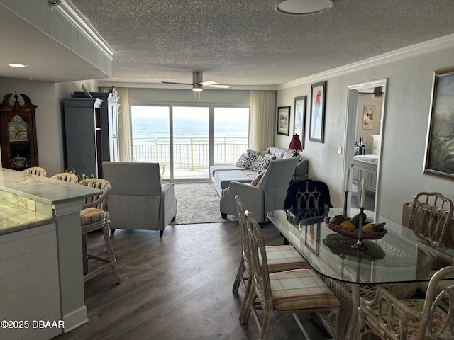 dining room with dark hardwood / wood-style flooring, ornamental molding, ceiling fan, a water view, and a textured ceiling