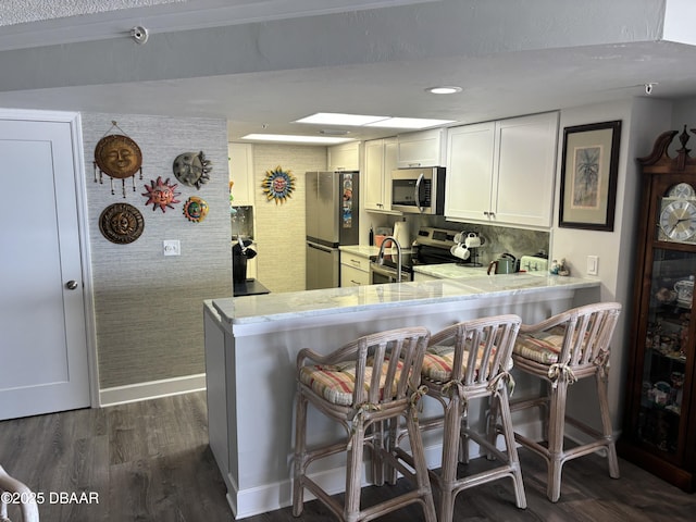 kitchen featuring appliances with stainless steel finishes, white cabinets, a kitchen breakfast bar, and kitchen peninsula