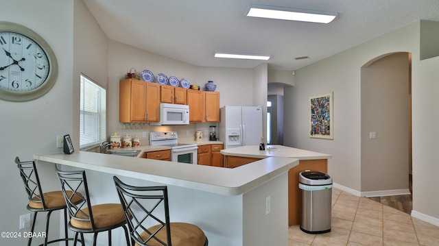 kitchen featuring kitchen peninsula, white appliances, light tile patterned flooring, and a breakfast bar area