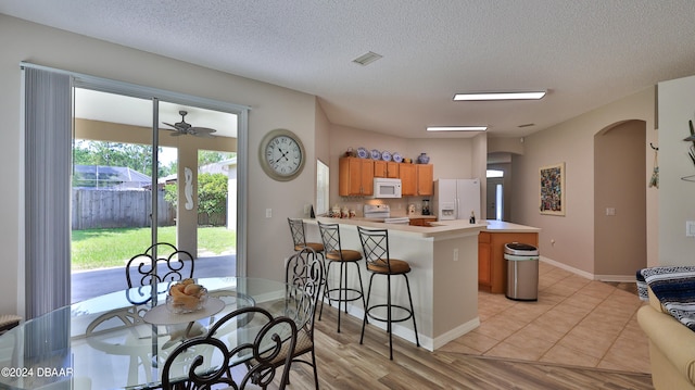 kitchen with light wood-type flooring, kitchen peninsula, white appliances, and plenty of natural light