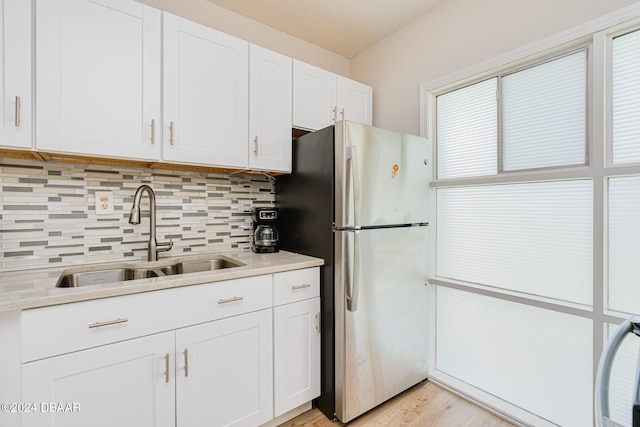 kitchen with a textured ceiling, sink, stainless steel refrigerator, and white cabinets