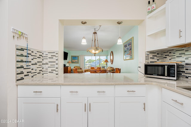 kitchen with light stone counters, backsplash, decorative light fixtures, white cabinets, and kitchen peninsula