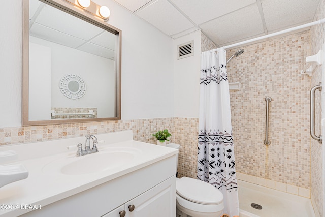 bathroom with tile walls, a paneled ceiling, vanity, a shower with shower curtain, and toilet