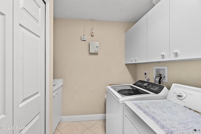 laundry room featuring cabinets, a textured ceiling, washer and clothes dryer, and light tile patterned flooring