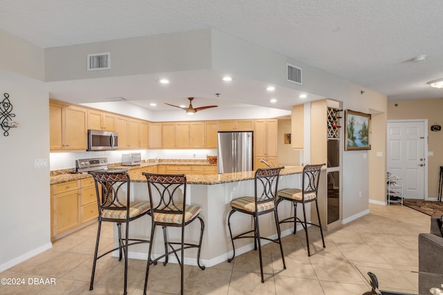 kitchen featuring light brown cabinets, light stone countertops, a textured ceiling, and appliances with stainless steel finishes