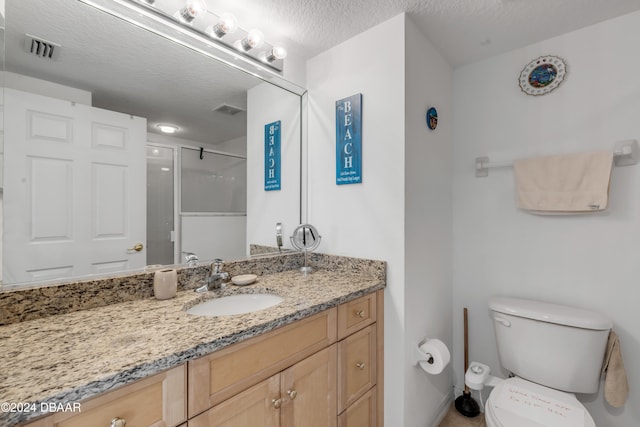 bathroom featuring toilet, vanity, a textured ceiling, and a shower with shower door