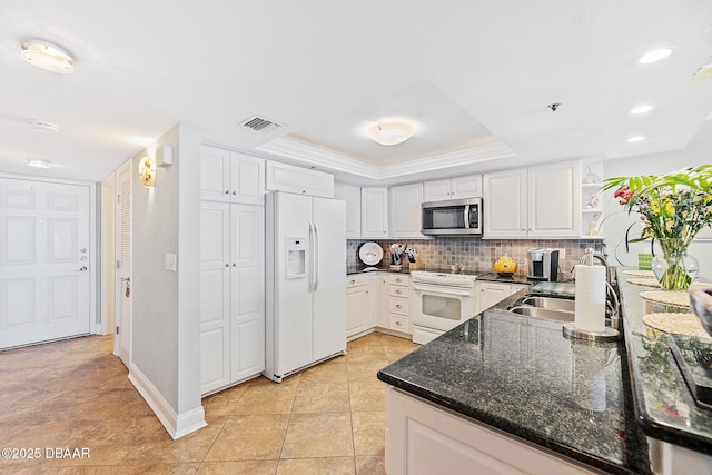 kitchen with white cabinets, decorative backsplash, dark stone counters, a raised ceiling, and white appliances