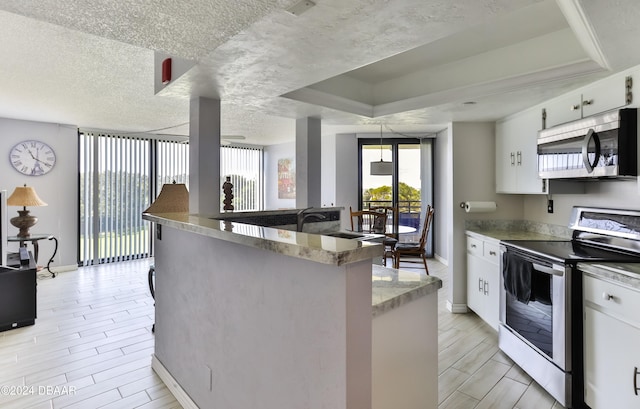 kitchen featuring white cabinets, light hardwood / wood-style flooring, a textured ceiling, a tray ceiling, and appliances with stainless steel finishes