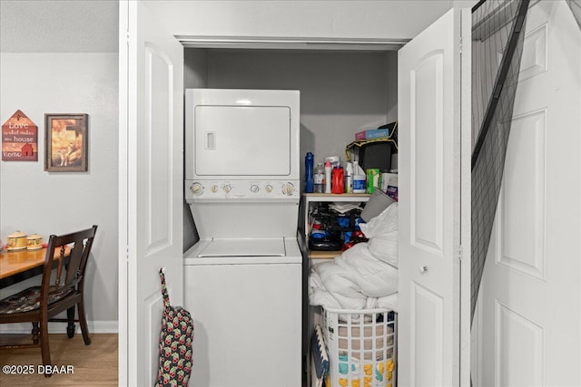 laundry room with laundry area, baseboards, stacked washer / drying machine, and wood finished floors