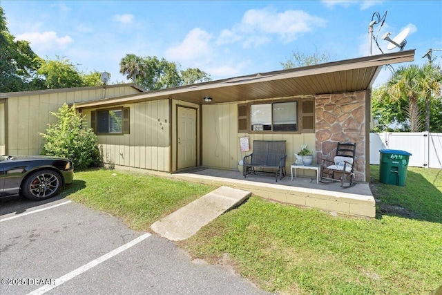 exterior space featuring stone siding, uncovered parking, fence, and a lawn