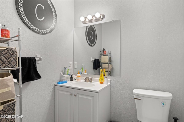 bathroom featuring toilet, a textured wall, and vanity