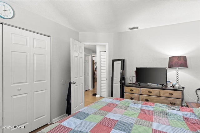 bedroom with a textured ceiling, a closet, light wood-type flooring, and visible vents