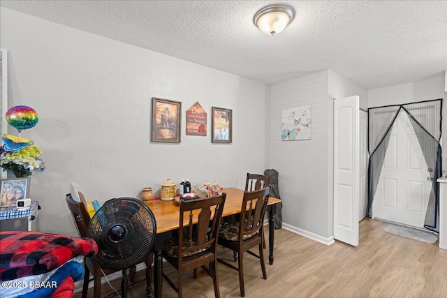 dining room featuring light wood-style flooring, baseboards, and a textured ceiling