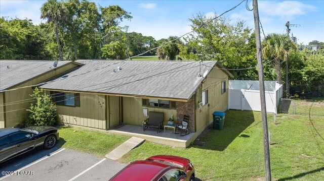 rear view of house with a yard, uncovered parking, a shingled roof, a patio area, and fence