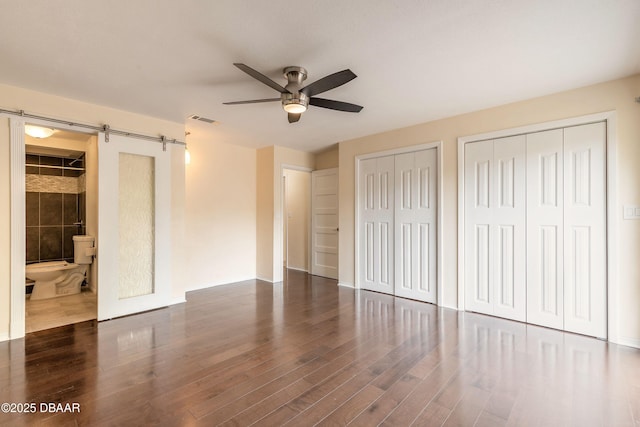 73 N St Andrews Dr, Ormond Beach, FL 32174 - unfurnished bedroom with a barn door, two closets, wood finished floors, and ceiling fan