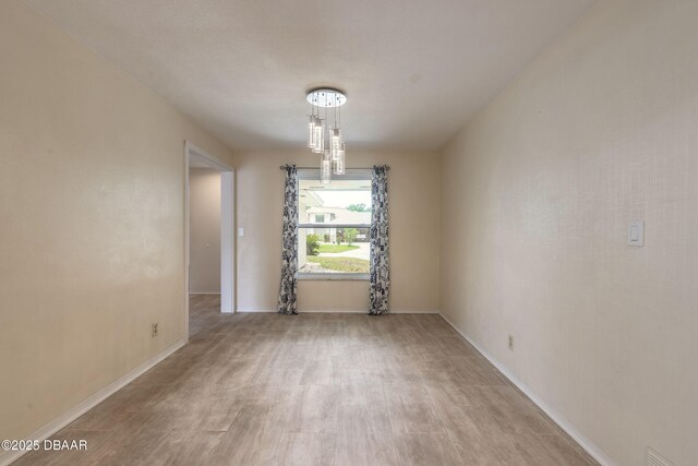 73 N St Andrews Dr, Ormond Beach, FL 32174 - unfurnished room featuring light wood finished floors, baseboards, and a chandelier