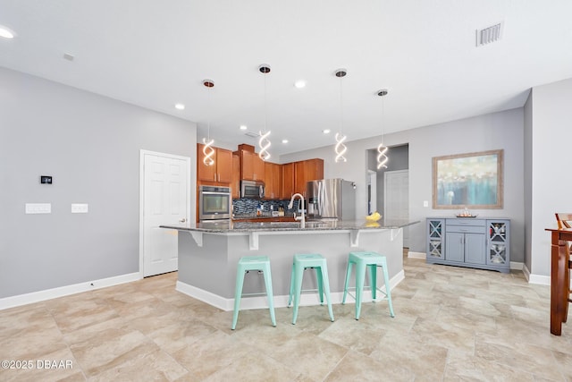 kitchen featuring a breakfast bar area, stainless steel appliances, visible vents, light stone countertops, and a center island with sink