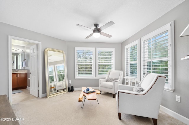 living area featuring baseboards, a ceiling fan, and light colored carpet