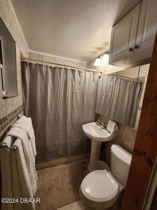 full bath with a textured ceiling, tile walls, toilet, and a shower with curtain