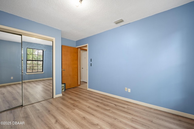 unfurnished bedroom with a textured ceiling, visible vents, baseboards, a closet, and light wood-type flooring