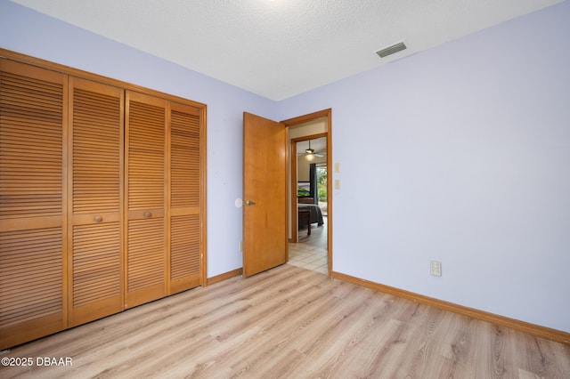 unfurnished bedroom featuring a textured ceiling, light wood-style flooring, visible vents, baseboards, and a closet