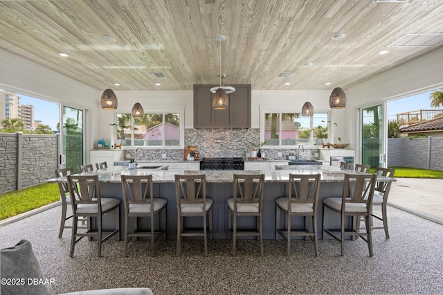 kitchen featuring a spacious island, wood ceiling, decorative light fixtures, light stone countertops, and a sink