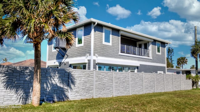 view of side of property featuring a balcony, a lawn, and fence