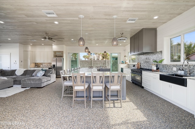 kitchen featuring range with two ovens, a sink, hanging light fixtures, a large island, and stainless steel fridge with ice dispenser