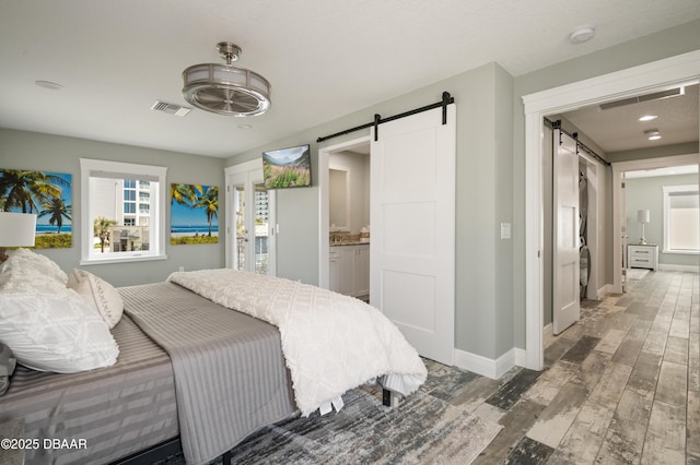 bedroom featuring a barn door, wood finished floors, visible vents, and baseboards