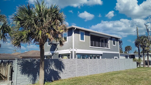 view of side of home featuring a balcony, fence private yard, and a lawn