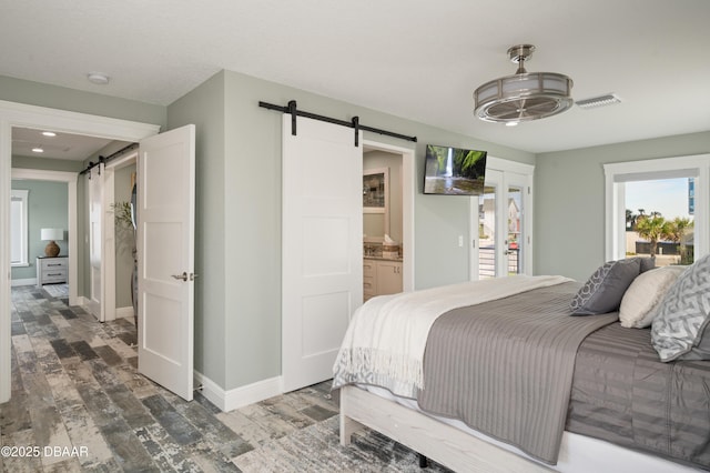 bedroom with wood finished floors, visible vents, baseboards, and a barn door