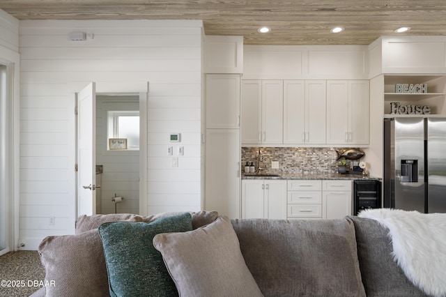 kitchen with stainless steel fridge, wine cooler, open floor plan, white cabinetry, and a sink