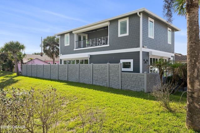 back of house featuring stone siding, a lawn, a balcony, and fence