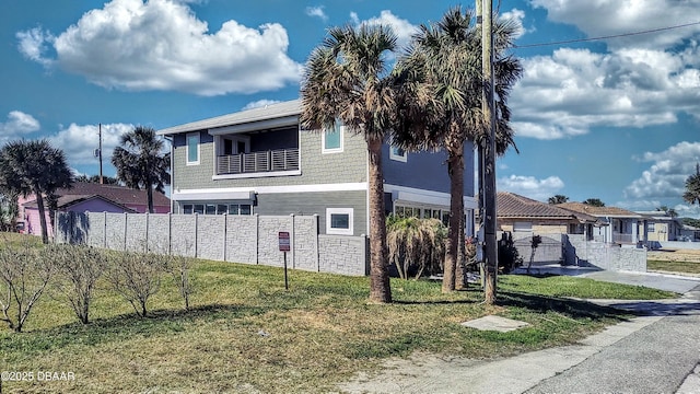 view of side of property with a lawn, fence, stone siding, and a balcony