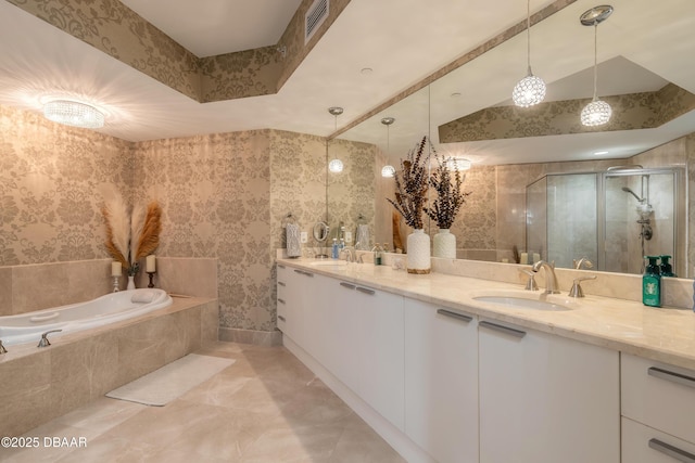 bathroom with a stall shower, double vanity, a sink, and wallpapered walls