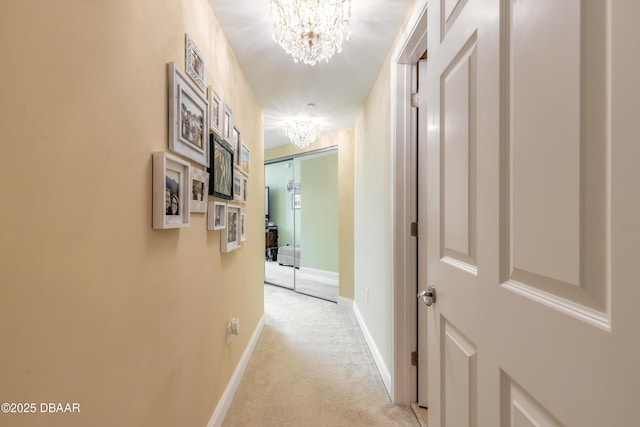 hallway with light carpet, baseboards, and an inviting chandelier