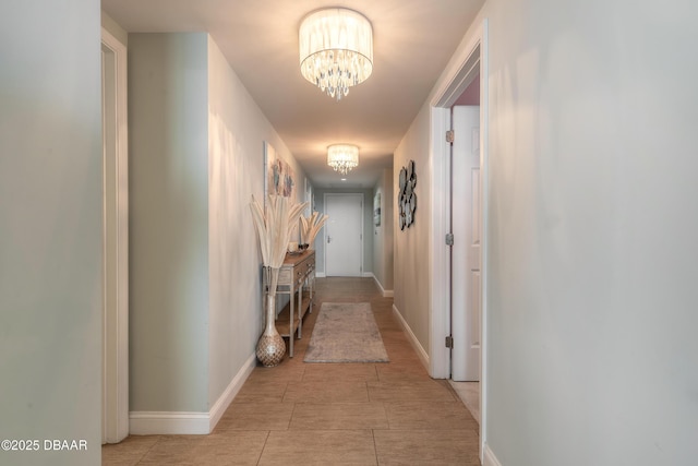 corridor with baseboards and a notable chandelier