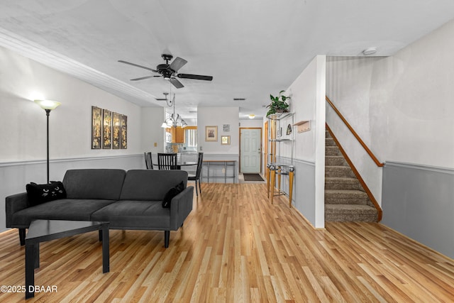 living area featuring light wood-type flooring, stairway, a ceiling fan, and baseboards