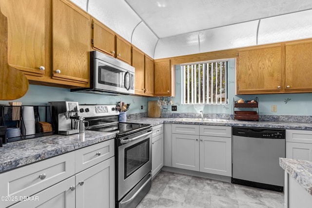 kitchen with appliances with stainless steel finishes, a sink, and brown cabinets