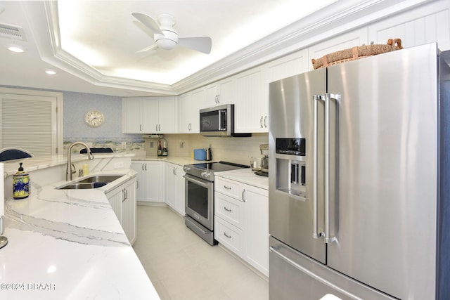 kitchen with sink, appliances with stainless steel finishes, light stone countertops, a tray ceiling, and white cabinets