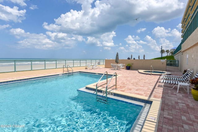 view of swimming pool with a patio, a water view, and a beach view