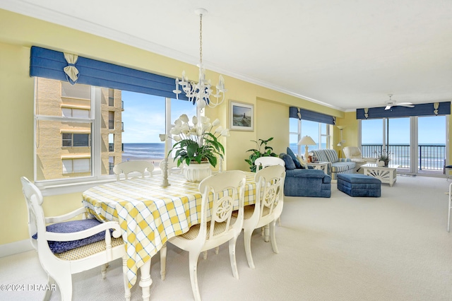 carpeted dining area with ornamental molding, ceiling fan with notable chandelier, a water view, and a healthy amount of sunlight