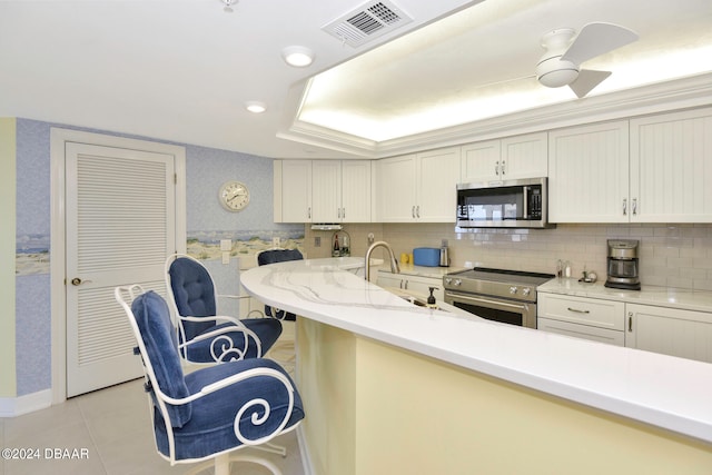 kitchen with stainless steel appliances, a kitchen breakfast bar, light tile patterned floors, backsplash, and white cabinets