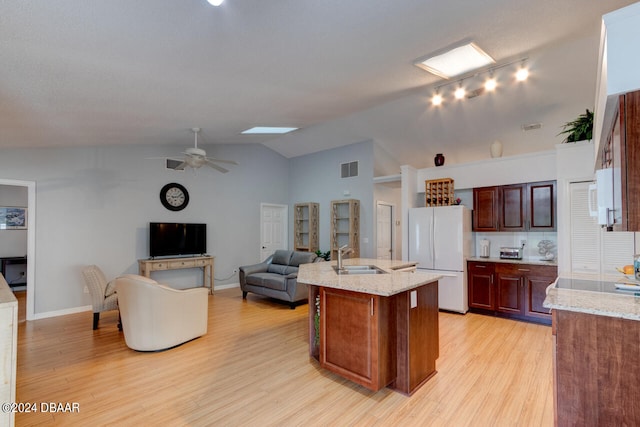 kitchen featuring light wood-style floors, freestanding refrigerator, a sink, an island with sink, and vaulted ceiling with skylight