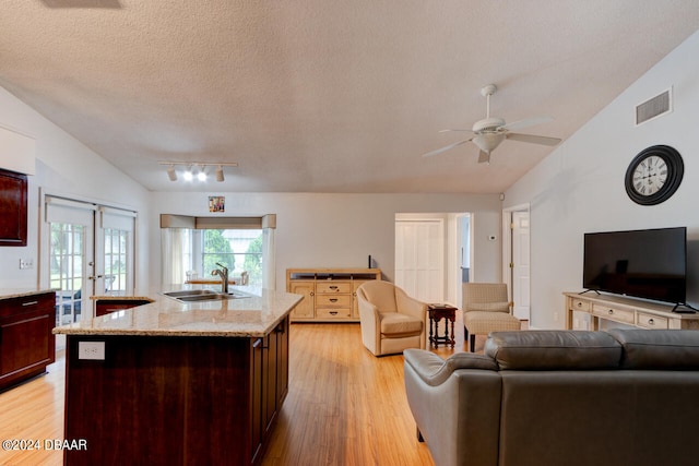 living area featuring lofted ceiling, visible vents, light wood-style flooring, and a textured ceiling