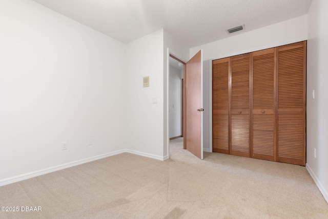 unfurnished bedroom with a textured ceiling, a closet, light colored carpet, visible vents, and baseboards